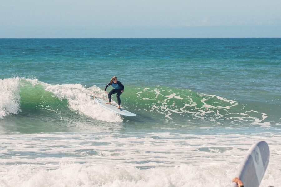 Surferin auf grüner Welle im Surfkurs von Mellowmove am Praia Azul in Portugal