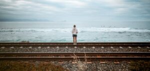 Frau an Bahngleisen am Meer mit Wellen und Surfern